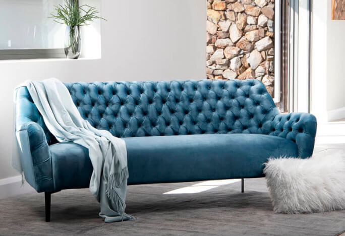 Classic styled velvet blue couch with buttoned back and arm rests in a modern living room setting
